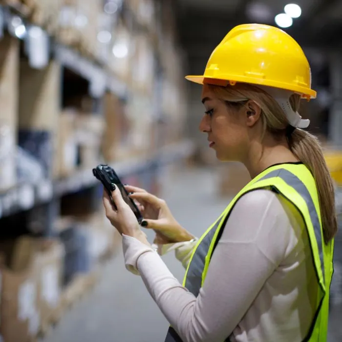 Warehouse worker in a hard hat scanning inventory with a handheld device