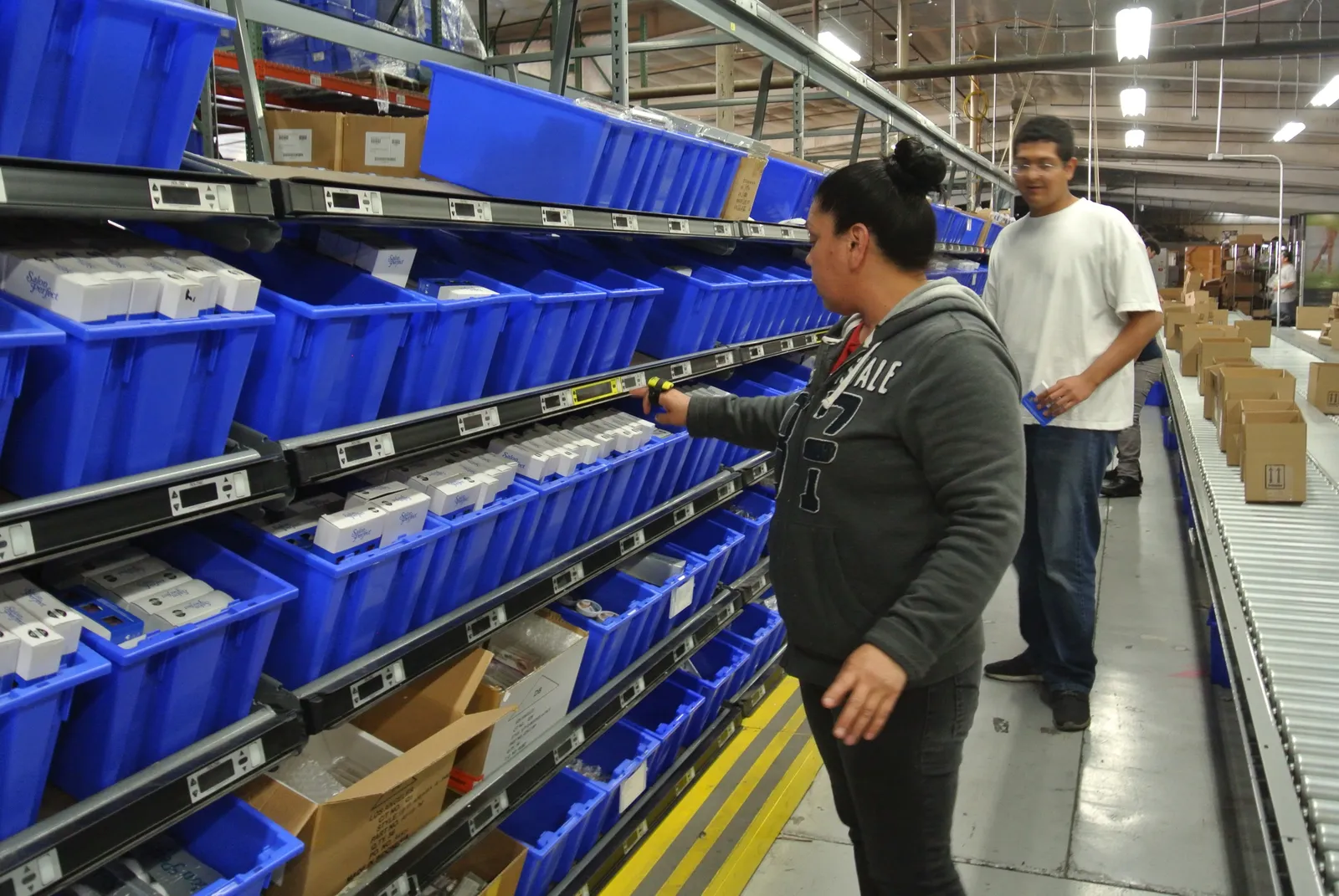 Warehouse operator pressing the confirmation button on a lit pick-to-light module while picking from blue bins on flow rack